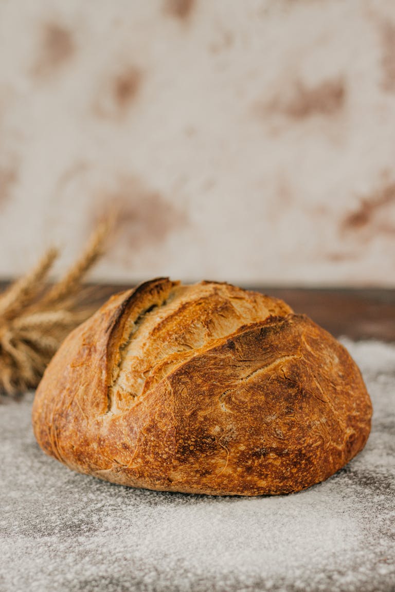 Freshly baked artisan bread loaf on a flour-dusted surface with wheat stalks.